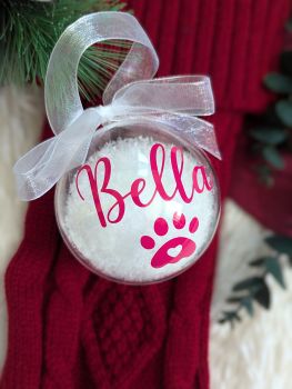 Celebrate your furry family member this holiday season with our Personalized Pet Christmas Bauble! Made from eco-friendly plastic and filled with festive snow, this 80mm bauble is a charming keepsake for years to come. Each bauble is customized with your pet's name (1 name only) and features a cute paw print, making it a thoughtful addition to your tree or a heartwarming gift. Complete with an organza ribbon and available in various vinyl colours, it&rsquo;s the perfect way to celebrate your dog&rsquo;s first Christmas!