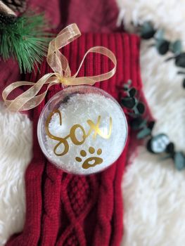 Celebrate your furry friend with our Personalized Snow-Filled Pet Christmas Bauble. Made from eco-friendly plastic, this 100mm bauble comes filled with festive snow and includes your pet's name and a paw print. Complete with an organza ribbon, it&rsquo;s the perfect keepsake for your tree or a thoughtful gift for a dog-loving friend!