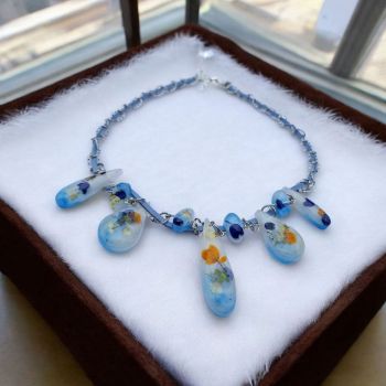 Nature-inspired necklace with 9 resin pendants containing dried wildflowers. Worn on a soft blue suede cord with chain. Adjustable 40–45 cm.
