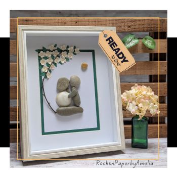 A beautiful ivory and green pebble art picture, showing a couple embracing under a tree with delicate pearl flowers and a glowing honey heart. A timeless piece, perfect for a wedding, engagement or anniversary gift. Ready to Ship.
This elegant handmade pebble art picture shows a loving couple embracing under a leafy green tree. The design has a soft ivory and green theme, with delicate flowers created from ivory paper and finished with warm pearls. A heart-shaped honey-coloured pebble sits above them, casting a gentle golden glow over their love – it could even be seen as a setting sun.
The bride’s dress is crafted with a natural shell skirt, adding a unique touch from the sea. The scene is framed with a coordinating green paper rim for balance and harmony, while the outer frame itself is a warm nude/sand colour with a crisp white inner rim – a combination that is both elegant and timeless.
This piece would make a truly special wedding gift, engagement present, or anniversary keepsake. It is part of my Ready to Ship range, meaning it is available now and will be posted quickly while still allowing it to be personalised with their names and chosen date.
Frame size: approx. 8 x 10"
Handmade with pebbles, shell, paper, pearls, and love
A thoughtful gift to celebrate love and new
beginnings.