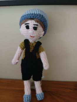 Crochet doll in black dungarees and blue beanie hat.