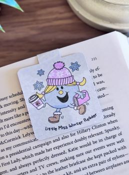 A sparkly handmade magnetic bookmark featuring a cheerful winter reader holding a hot drink and a book. The design is covered in a beautiful glitter effect with the text&nbsp;&ldquo;Little Miss Winter Reader.&rdquo;&nbsp; A lovely stocking filler or winter gift for book lovers.