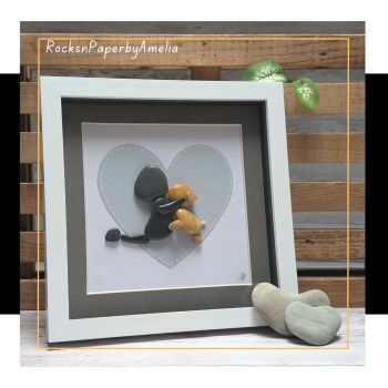 Celebrate the timeless bond between a girl and her beloved dog with this heartfelt piece of pebble art. The girl is shown kneeling, embracing her loyal companion, perfectly positioned within a soft light grey heart against a clean white background. This simple yet striking design evokes feelings of warmth, love, and connection.