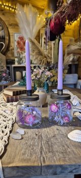 Enchanting boho-cottagecore candle holders made from classic glass mason jars filled with delicate dried everlasting flowers (strawflowers and blooms in soft pinks, vibrant purples, lilacs, and whites) arranged whimsically with airy stems and petals for a preserved, ethereal look.