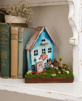 A unique miniature house handcrafted from reclaimed wood and hand-painted with acrylics. This whimsical piece features a lush garden of moss, delicate dry flowers, and tiny clay mushrooms. Perfectly detailed on every side, it's a tiny world designed to bring a touch of fairytale charm to your home.&nbsp; 15/9/17 cm.