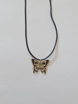 A black and gold enamel charm of a butterfly shape with a golden skull design within the wings of the insect. The charm is on a black rope necklace