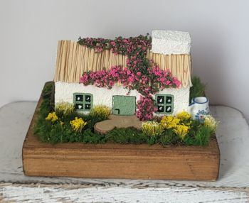 Capture Irish charm with this handcrafted miniature cottage, featuring a traditional thatched roof, green-trimmed windows and a blooming floral facade! 11/8/7 cm perfect for any shelf or a perfect gift!