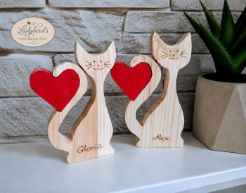 A beautiful, freestanding wooden cat couple decor set, custom engraved with your chosen names. This 2-piece interlocking set comes with two vibrant red wooden hearts that fit perfectly into the cats' tails, symbolising love and connection. It makes the perfect heartfelt gift for anniversaries, Valentine's Day, weddings, or for any cat-loving couple. What makes this piece truly special is that the names are meticulously hand-burned (pyrography) onto the wood by hand, giving each cat a unique, textured artisan finish. No lasers or machines are used.
⚠️ SAFETY NOTICE: This product is designed as a home decor item only. It is NOT a toy and is NOT suitable for children to play with. 
⚠️ HOW TO ORDER: In the personalisation box below, please enter the two names you would like to be hand-burned onto the cats, clearly stating the names for the larger and smaller cat.
Example format: &bull; Larger Cat: Alex &bull; Smaller Cat: Gloria