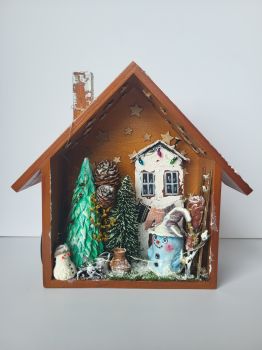 Beautiful 18,5/7.5/23 cm, this unique winter scene is in a wooden, shadow box, features an air-dry clay snowman, a forever green tree, a wooden house, and many miniature items for a cozy, frosty Christmas scene.