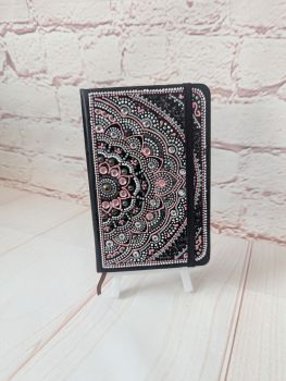 A small lined, undated notebook with a hand-painted black and pink mandala design.