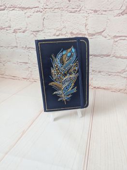 A small lined, undated notebook with a hand-painted blue and gold feather design on a dark blue cover.