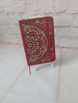 A lined, undated notebook with a hand-painted red mandala design, finished with metallic details and rhinestones. Compact, decorative, and practical for everyday notes.