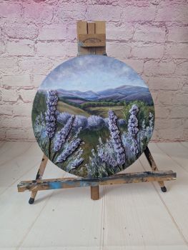 A 30 cm round landscape painting in acrylic, finished with raised handmade clay lavender details. Unframed.