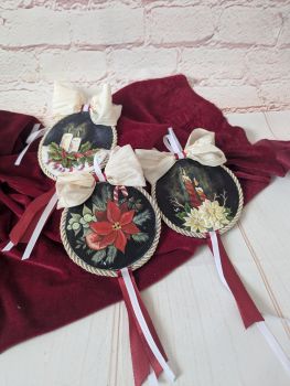 A set of three hand-painted Christmas ornaments featuring poinsettias and festive candle designs, presented in a gift box.